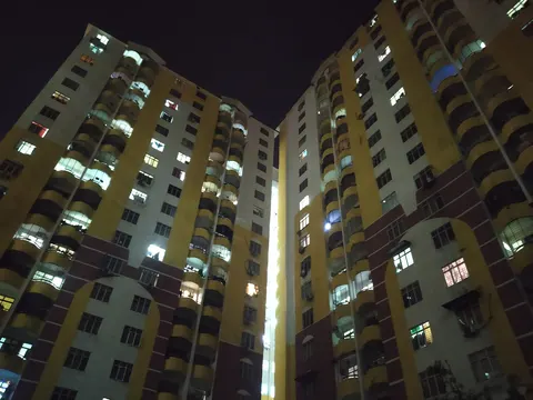 Lagoon Perdana: Two high-rise residential buildings with yellow and white facades and curved balconies, viewed from a low angle at night.