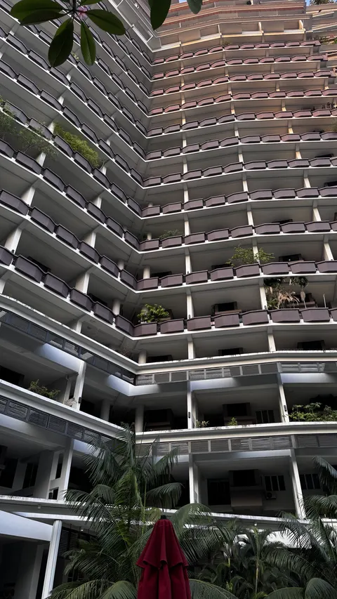 Armanee Terrace: A view of the white facade of a residential building with rows of dark balconies, seen from a lower courtyard level with tropical plants.