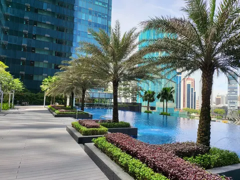 The Ritz-Carlton Residences, Kuala Lumpur: A rooftop infinity pool with palm trees and landscaped planters, set against a backdrop of modern skyscrapers.