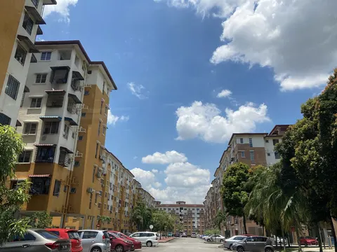Pangsapuri Tainia: A street-level view looking down a road between two rows of multi-story apartment buildings under a bright blue sky with scattered clouds.