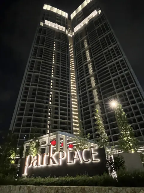 Park Place: A night photograph looking up at the facade of a tall residential tower with lit windows, featuring a brightly illuminated 'park PLACE' sign in the landscaped foreground.