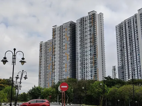 Parkhill Residence Bukit Jalil: A street-level view of several high-rise residential towers with white and grey facades, accented with yellow stripes, under an overcast sky, with a red car and street lamps in the foreground.