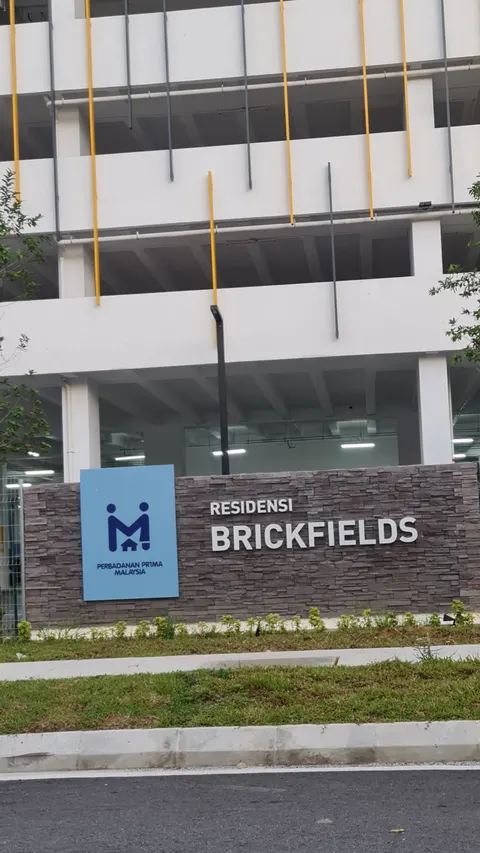 RESIDENSI BRICKFIELDS: A view of the entrance signage for Residensi Brickfields featuring a blue corporate sign and white letters on a stone wall, set against a multi-story parking structure.