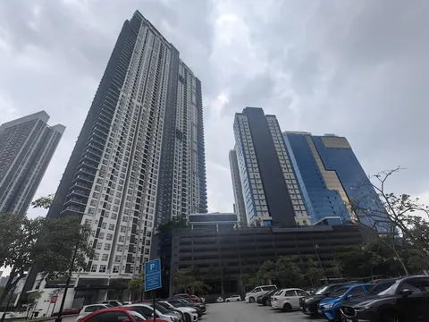 Met 1 Residences: A low-angle shot of several high-rise residential and office towers, including the dark and white tower on the left, standing over a parking lot filled with cars.