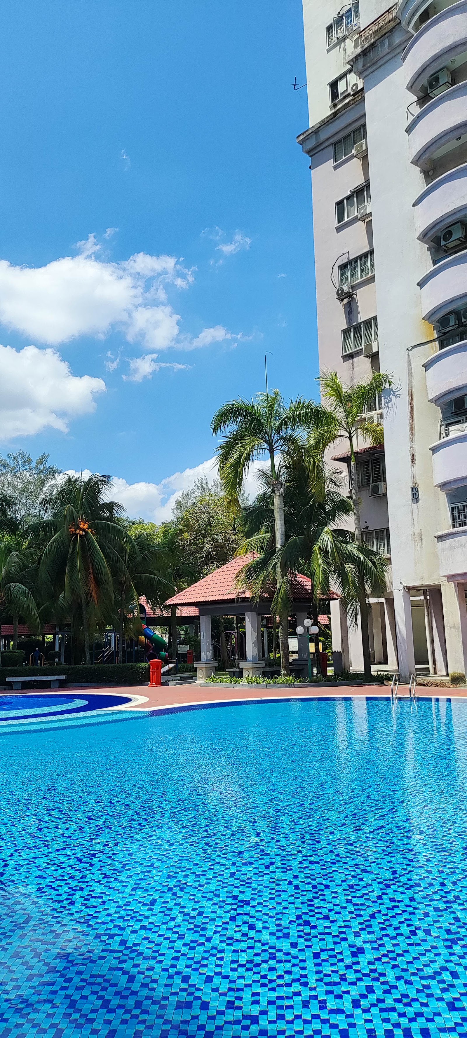 Ridzuan Condominium: An outdoor swimming pool with a tiled deck, situated next to a residential condominium building and palm trees.