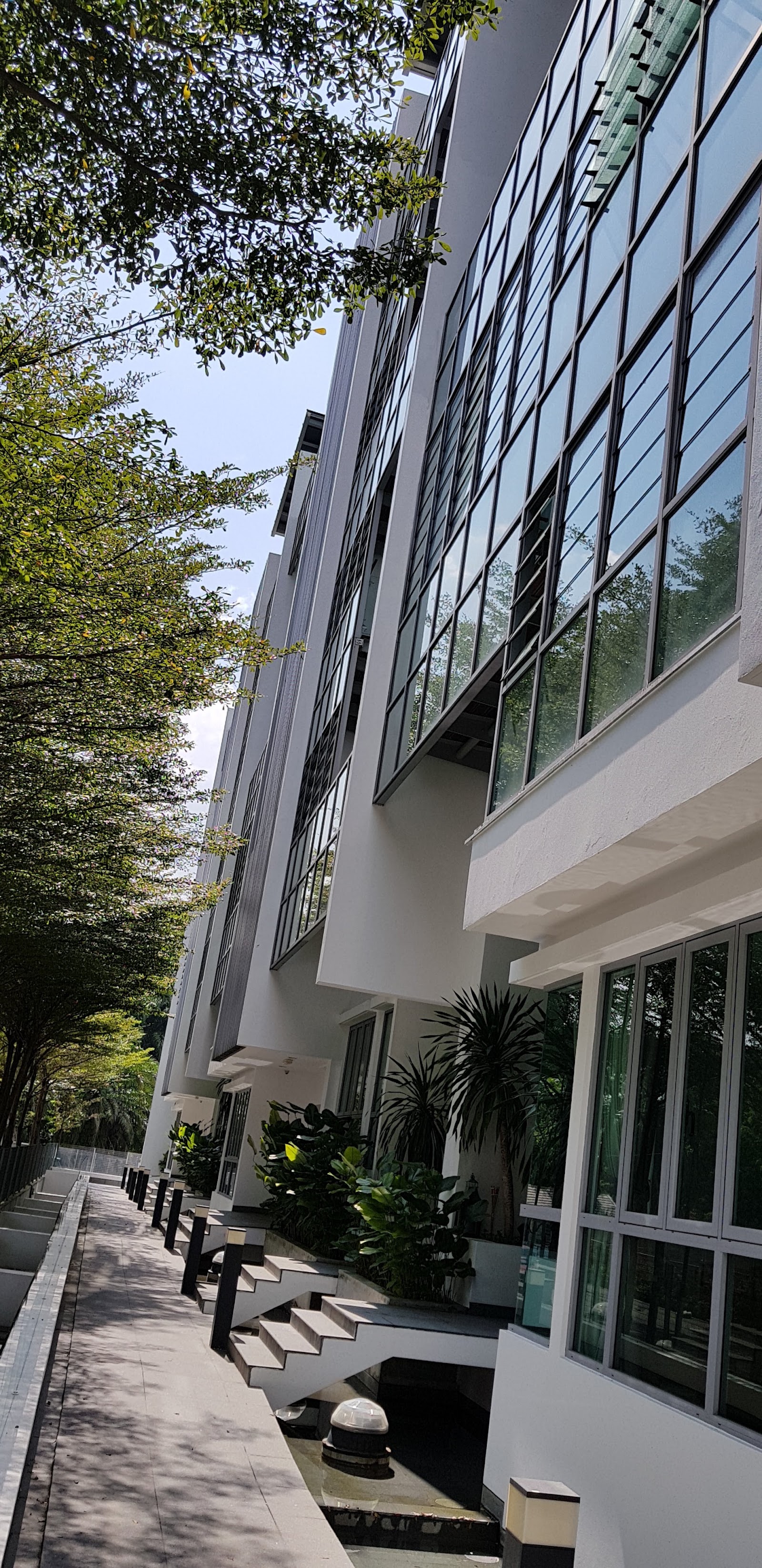 Amarin Wickham: A low-angle view of a white building facade with large glass windows, seen from an adjacent walkway and landscaping.