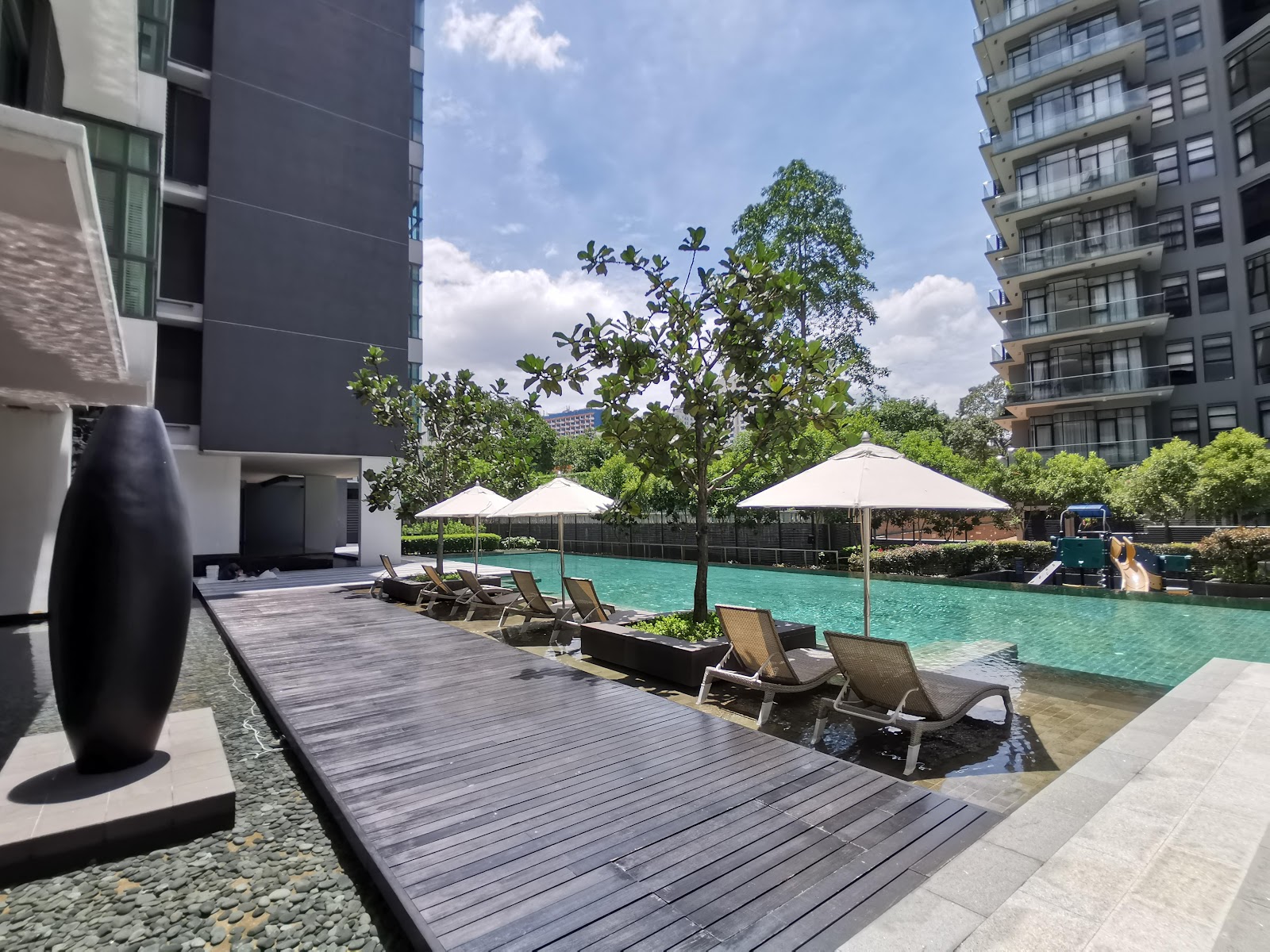 Madge Mansions Condominiums: A swimming pool area with lounge chairs, sun umbrellas, and a wooden deck, situated between modern residential towers.