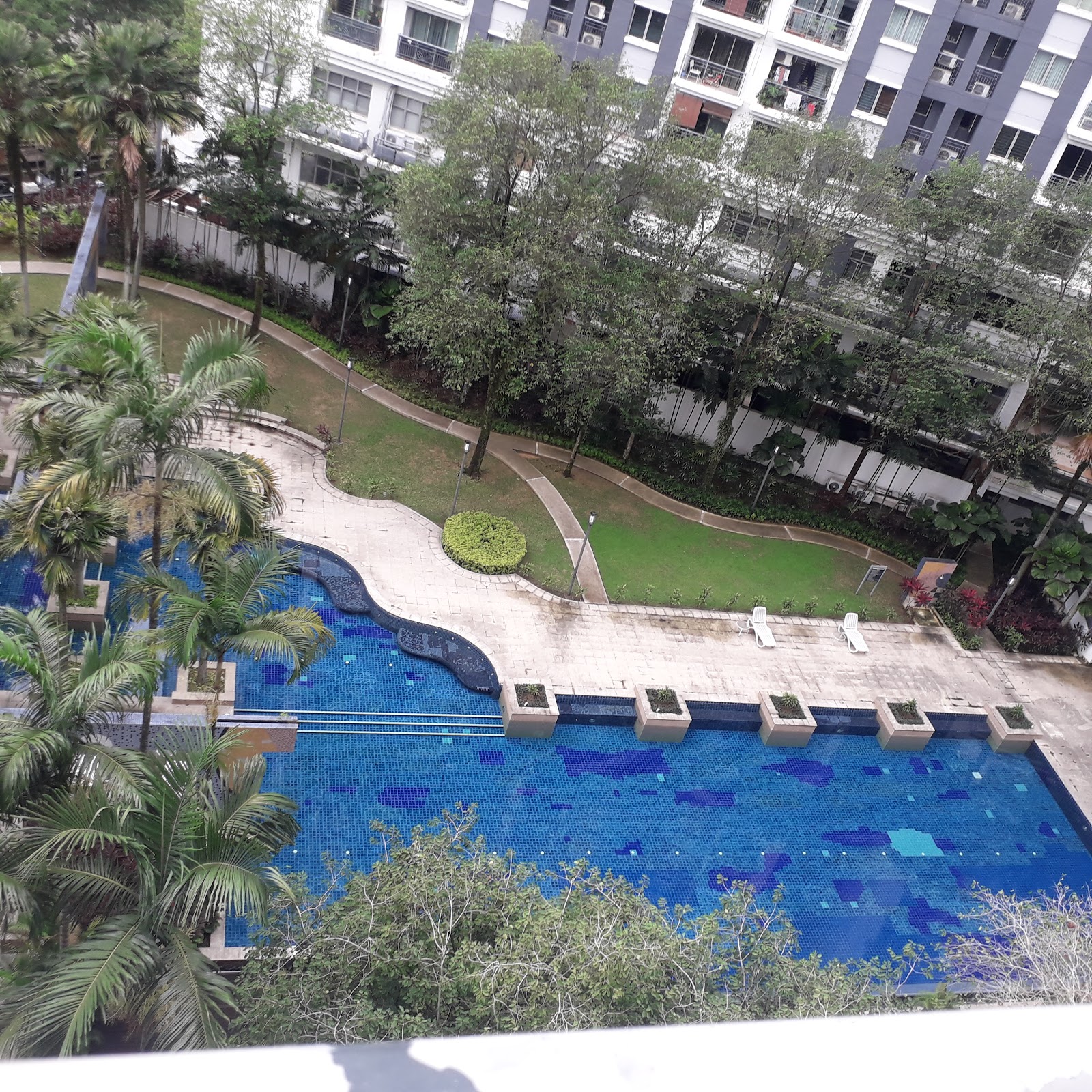 Emerald Serviced Apartment: An aerial view of a swimming pool with blue tiles, palm trees, and a paved walkway within a residential complex.