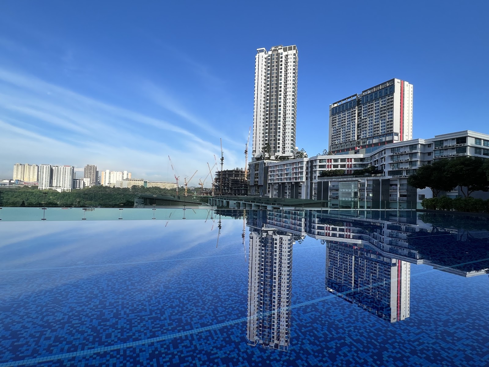 SUNWAY GEO RESIDENCES: A sky-high infinity pool with blue tiling reflecting the city skyline and surrounding high-rise buildings under a clear blue sky.