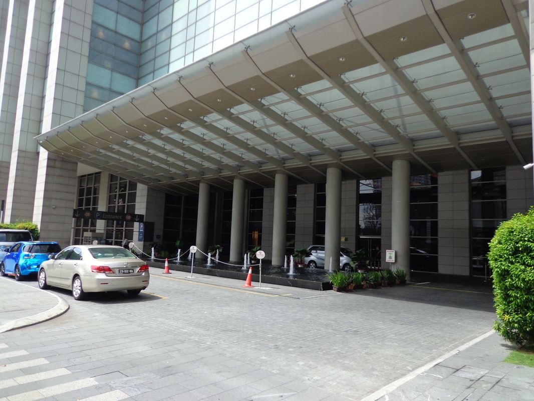 Pavilion Residences: A beige sedan is parked in front of the main entrance of a modern building with a large glass canopy and fountain.