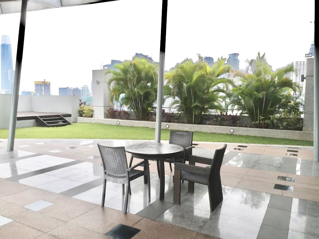 Gallery @ U-Thant: A rooftop terrace with a table and chairs, manicured lawn, and tropical plants against a city skyline backdrop.