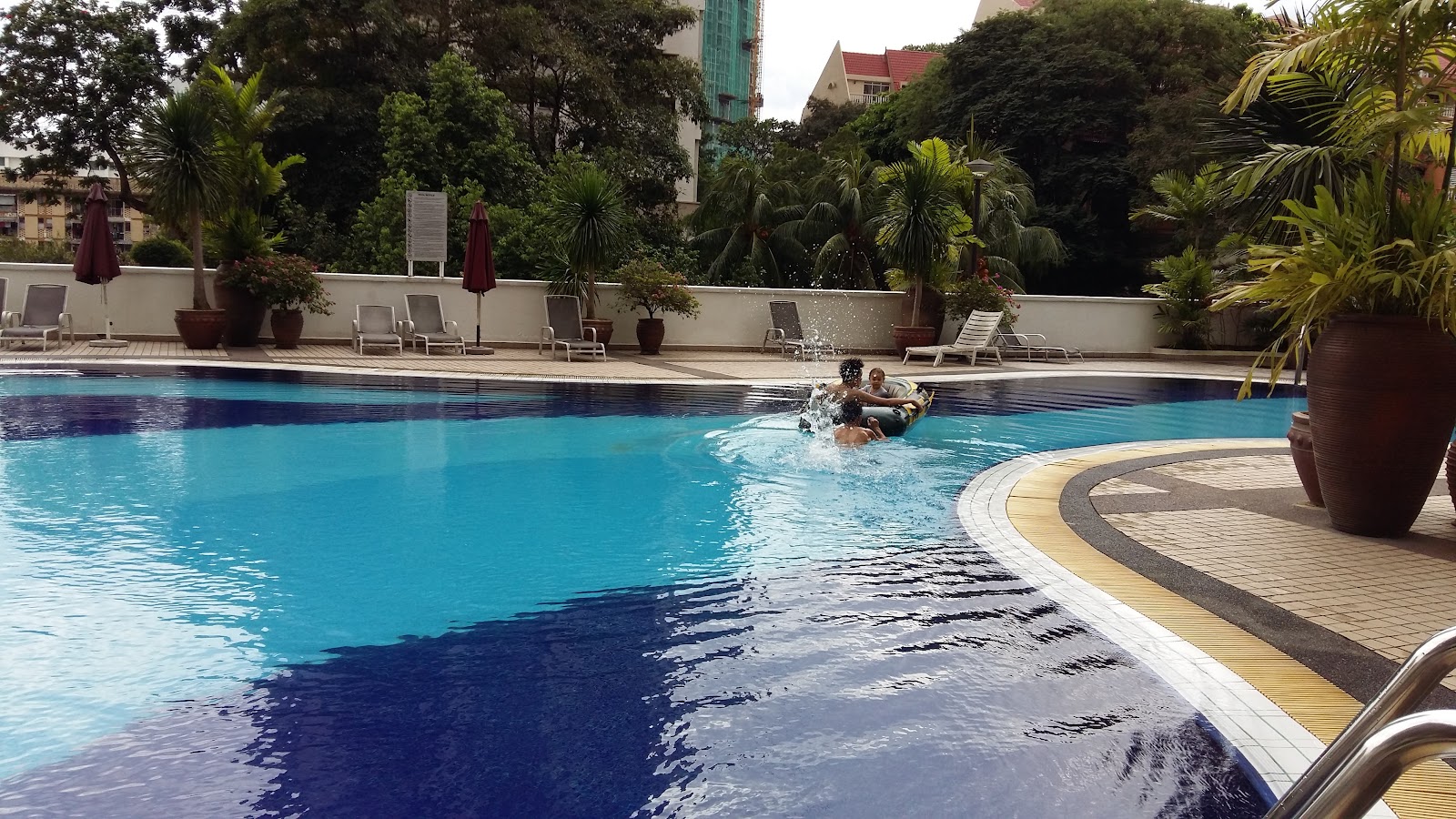 Angkasa Impian 2: A swimming pool with a group of people splashing in the water, surrounded by lounge chairs and potted plants.
