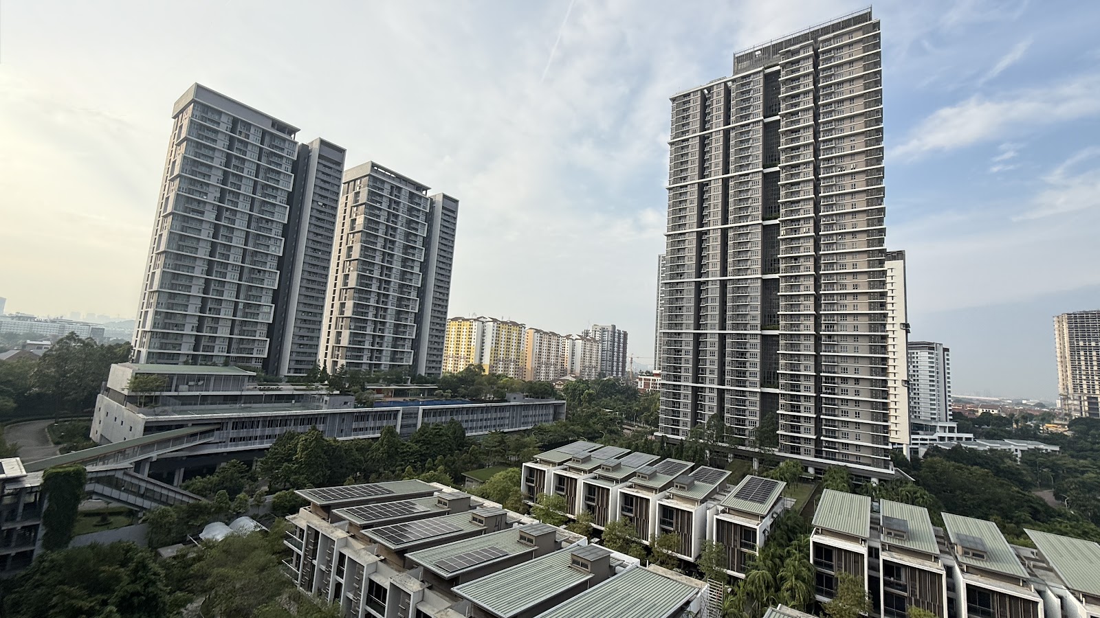 SUNWAY GEO RESIDENCES: A wide-angle view of a modern residential development featuring high-rise apartment towers and low-rise shophouses surrounded by trees.