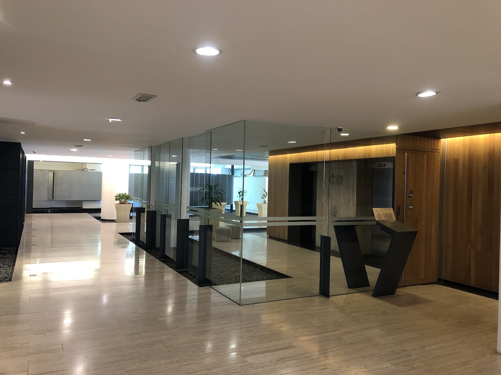 2 Hampshire: A modern interior lobby featuring a glass partition, a sleek black reception desk, and a wooden-paneled wall surrounding the elevator bank.