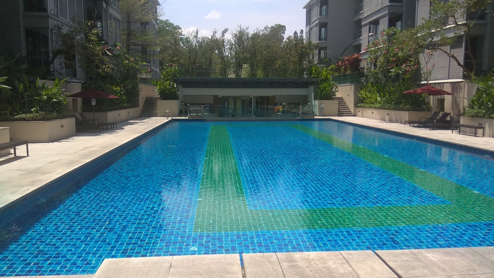 U-Thant Residence: A long, rectangular swimming pool with blue and green tiles at a residential development, surrounded by lounge chairs and landscaping.