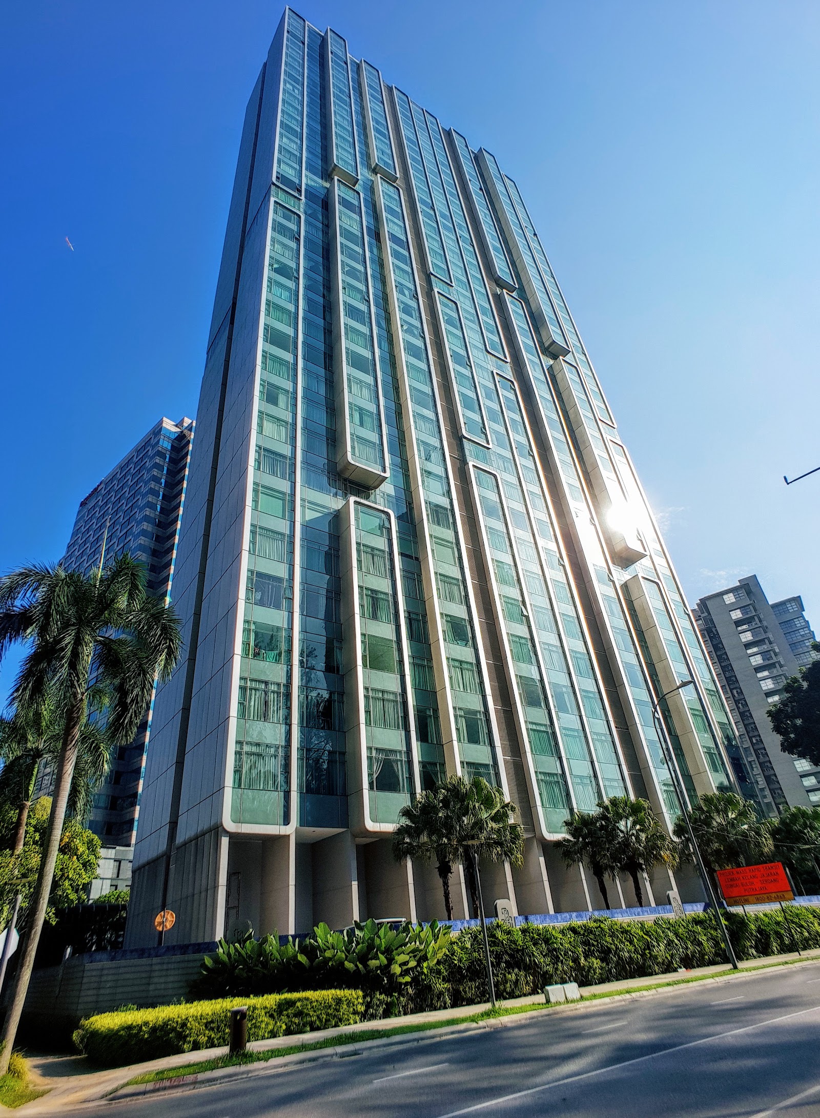 Quadro Residences: A low-angle exterior shot of a tall residential building with a modern glass facade and protruding bay window sections, set against a blue sky with palm trees in the foreground.