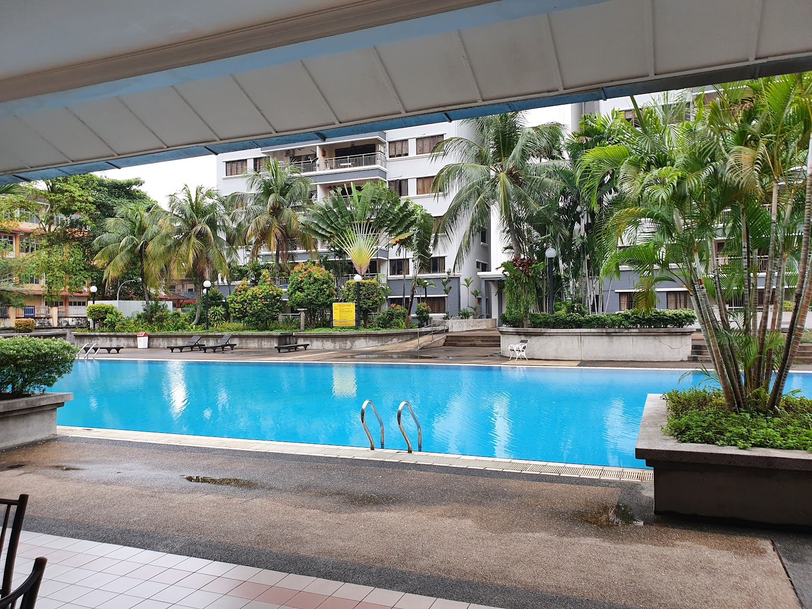 Menara Duta 1: A swimming pool surrounded by sun loungers and tropical landscaping, with residential apartment blocks in the background.