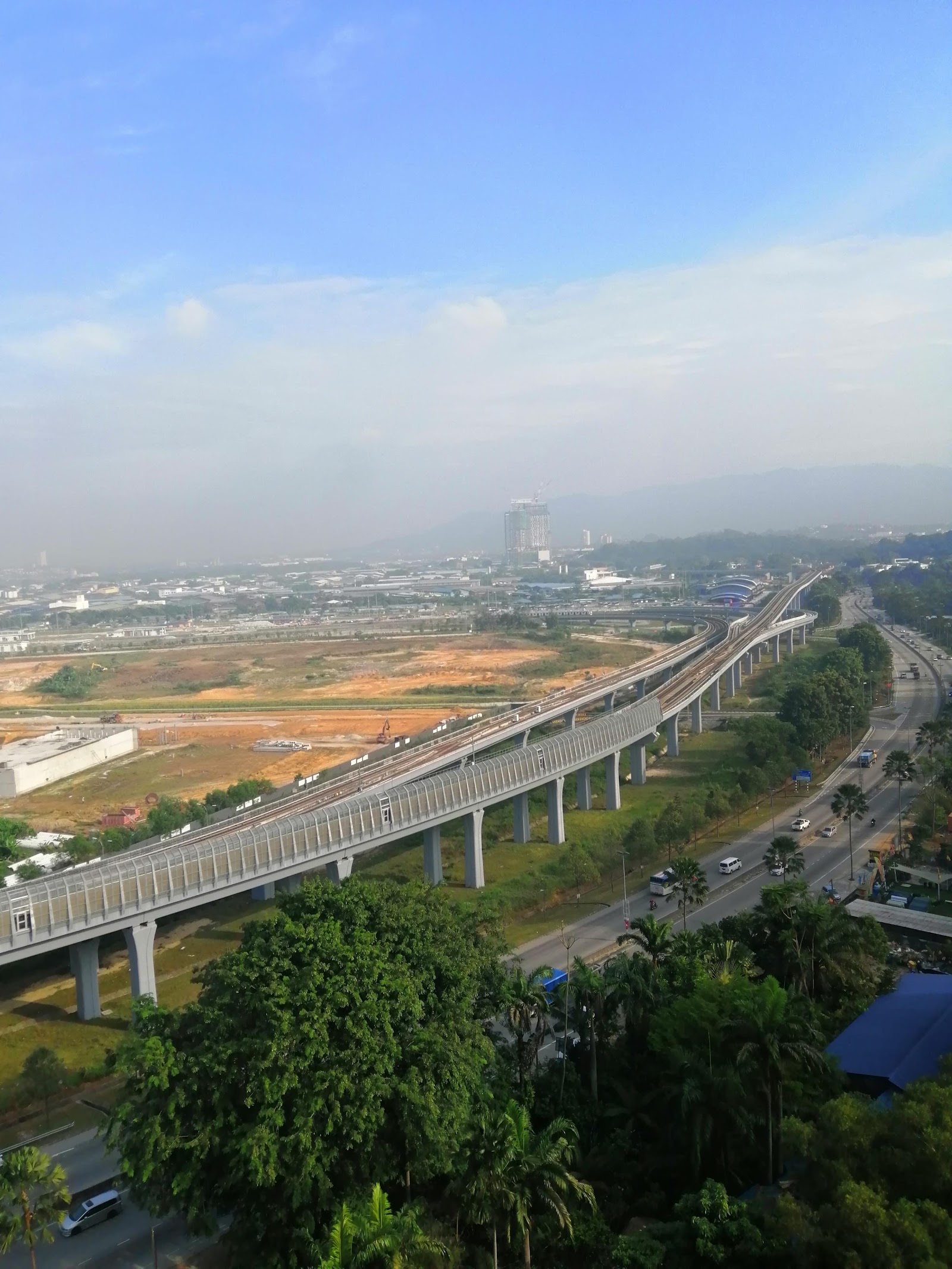Kasturi Idaman: An elevated view of an urban landscape featuring a high-speed rail viaduct, a road, and a city skyline in the distance under a clear sky.