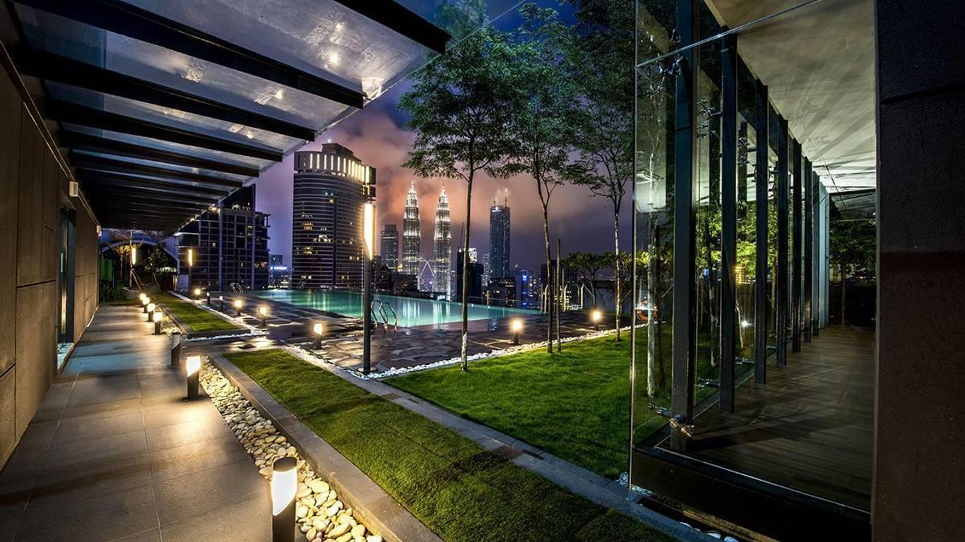 Dorsett Residences Bukit Bintang: A landscaped rooftop terrace with an infinity pool and walkways, overlooking a city skyline with prominent twin towers at dusk.