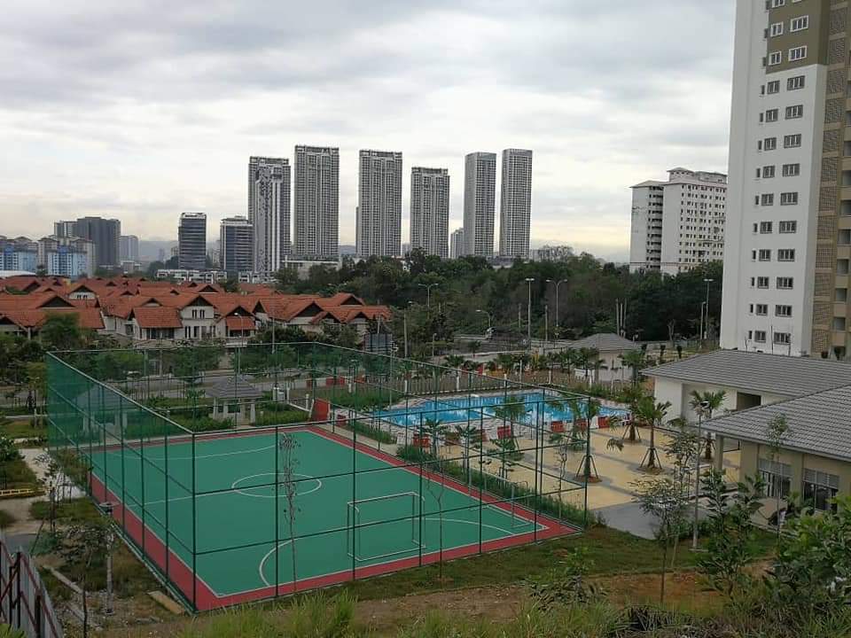 Condominium Akasia Bukit Jalil: A view of community amenities featuring a green and red sports court and a blue swimming pool, with residential buildings and distant high-rises in the background.