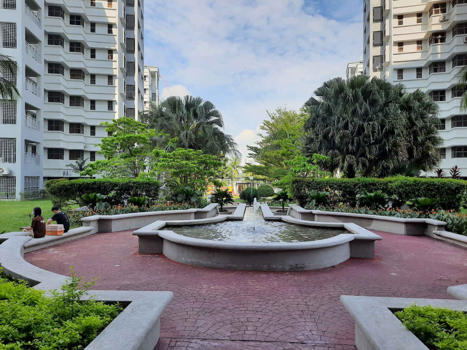 PALMVILLE RESORT CONDOMINIUM: A landscaped garden within a residential complex featuring a central concrete fountain, curved seating, and manicured greenery, with high-rise apartment blocks in the background.